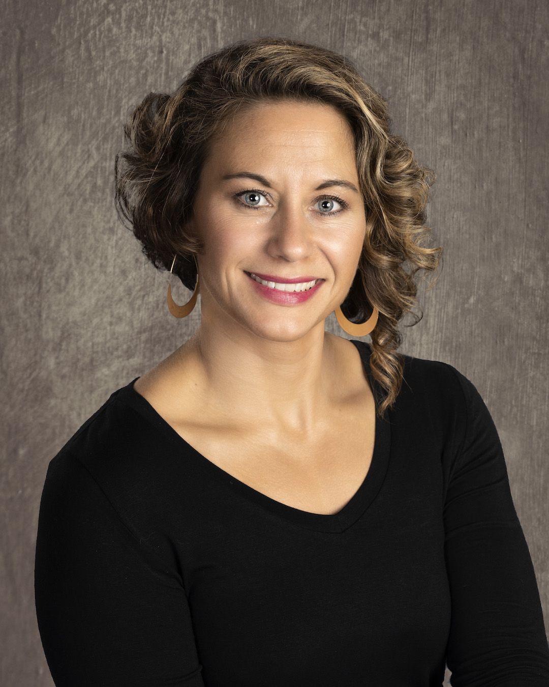 Angela Shuey, therapist, in a black v-neck against a warm grey studio backdrop